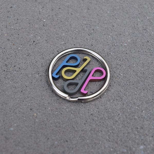 Set of colorful Pry.Me titanium bottle openers in blue, yellow, and pink, arranged on a keyring, showcasing their compact size and stylish anodized finish.