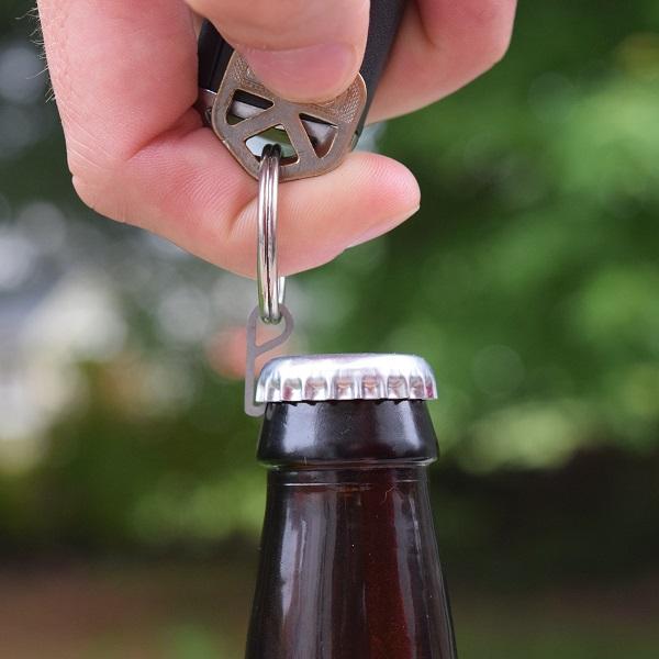 Pry.Me titanium bottle opener in action, opening a bottle attached to a keyring, highlighting its compact and durable design.
